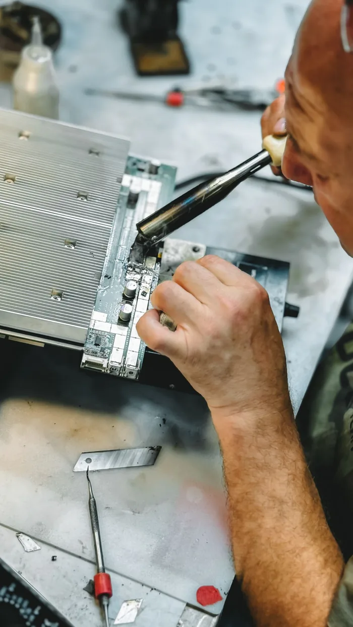 A technician soldering components on a television panel driver board